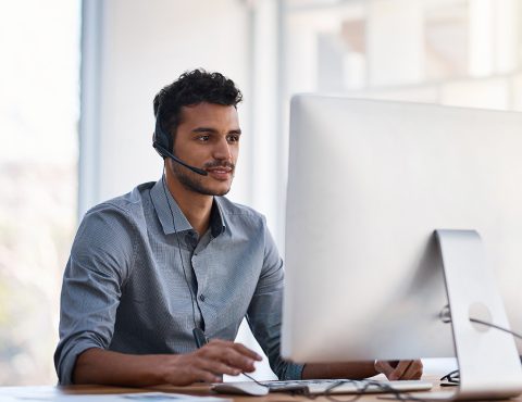 A person with a headset sitting behind a desk with a computer on it.