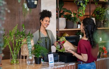 Two people in a shop. One person looks like they work there. The other is buying flowers from the shop.