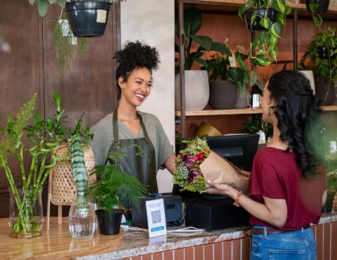 Two people in a shop. One person looks like they work there. The other is buying flowers from the shop.