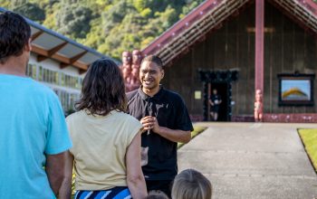 Several people standing in the front of a Māori cultural building called a Mara.