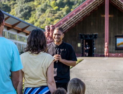 Several people standing in the front of a Māori cultural building called a Mara.
