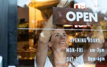 A smiling café worker in a striped apron hangs an 