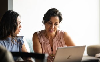 Two people sitting down and looking at a laptop.