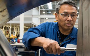 A person holding a tool and fixing the inside of a airplane turbine.
