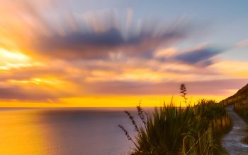 A lighthouse on a hilltop with the sunsetting in the background.