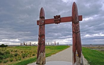 The entrance of a cultural Māori carving. In the background is a path that leads to the beach.