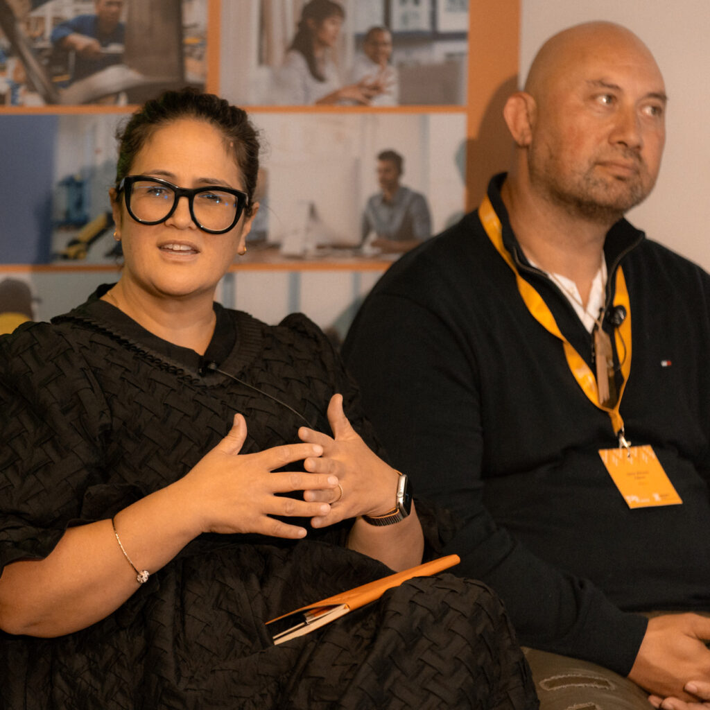 Two panelists are seated on stage, with one woman actively speaking and gesturing. A large Ringa Hora banner is displayed behind them.