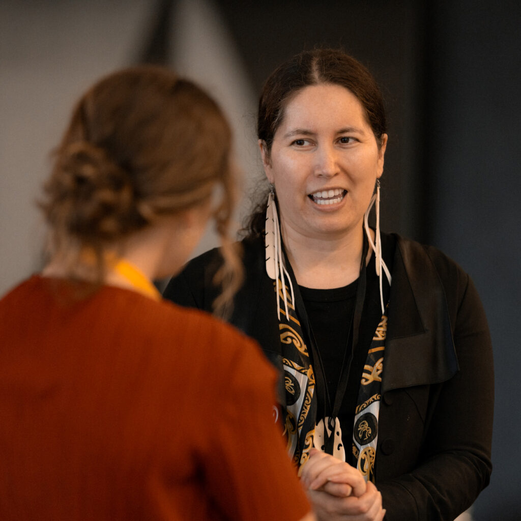 Two women in conversation, one facing forward with long white earrings and expressive hand gestures.