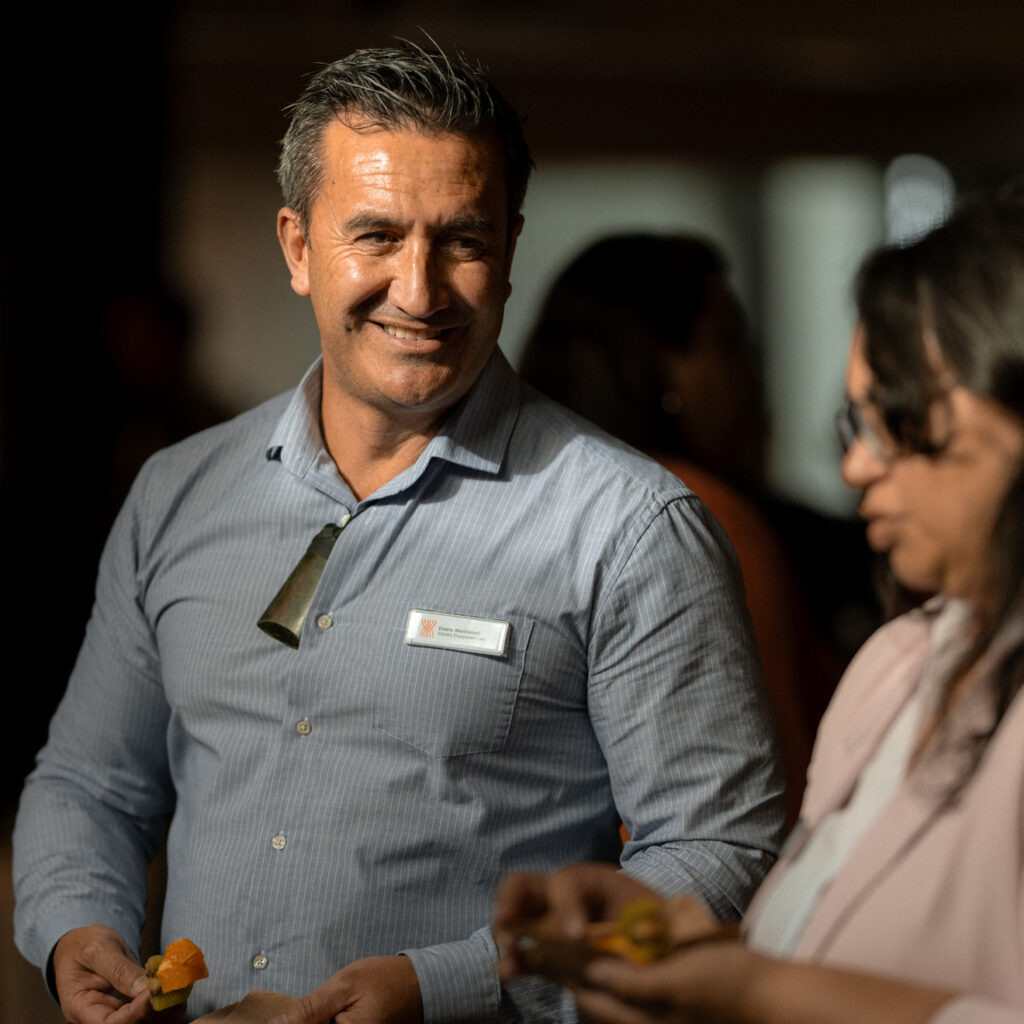 A smiling man in a blue shirt talking with a woman in a pink blazer at a social event.