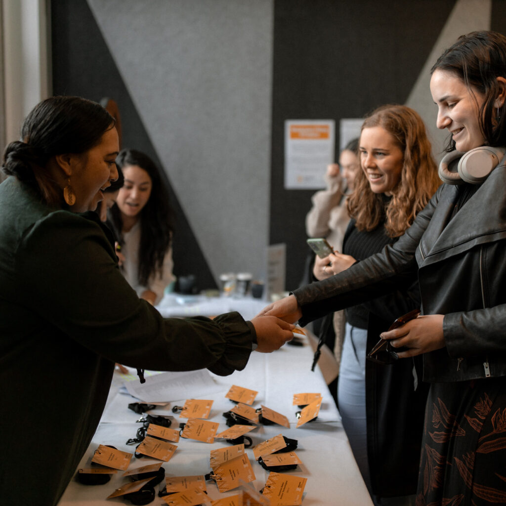 A woman handing out name badges at a table while others smile and engage in conversation.