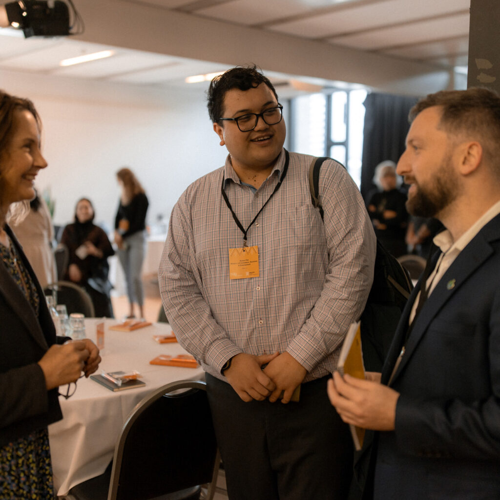 Three people talking, with one person smiling broadly while holding a notebook.