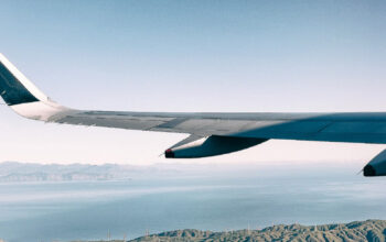 Close-up view of an airplane wing seen from a passenger window during flight, with the ocean and mountains below.
