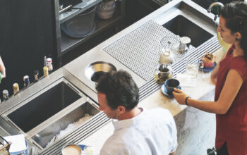 Top-down view of three people working behind a counter in a cafe or bar, preparing drinks and interacting.