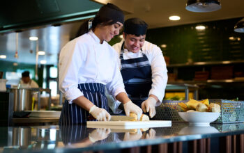 Two student chefs looking down and cutting bread.