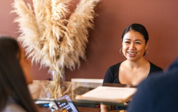 Three people at.a desk. One is smiling at the other who who are standing in front of the desk.