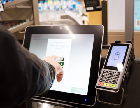 A close up of a person pointing at. a self checkout machine.