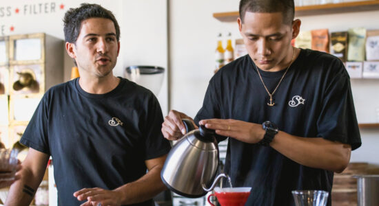 Four people in a coffee shop watching one person pour hot water in to a cup.
