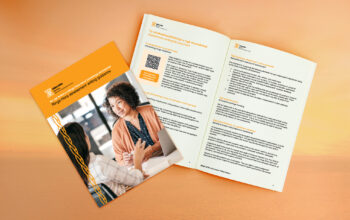 A Ringa Hora assessment writing guidance booklet placed on a wooden surface. The cover features a photo of two people having a discussion, with the title 'Ringa Hora assessment writing guidance' in orange text. The booklet is open, showing pages with headings, bullet points, a QR code, and bilingual text in English and Māori. The design includes an orange and white color scheme with woven decorative elements.