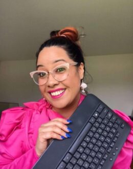 A close up of a person smiling while holding a keyboard in their hands. They are wearing a bright pink dress.
