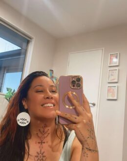 A person taking a photo of themselves in the mirror. They appear to be in a small room with a window and door in the background.