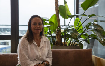 A women sitting down. In the background is a vibrant green pot plant.