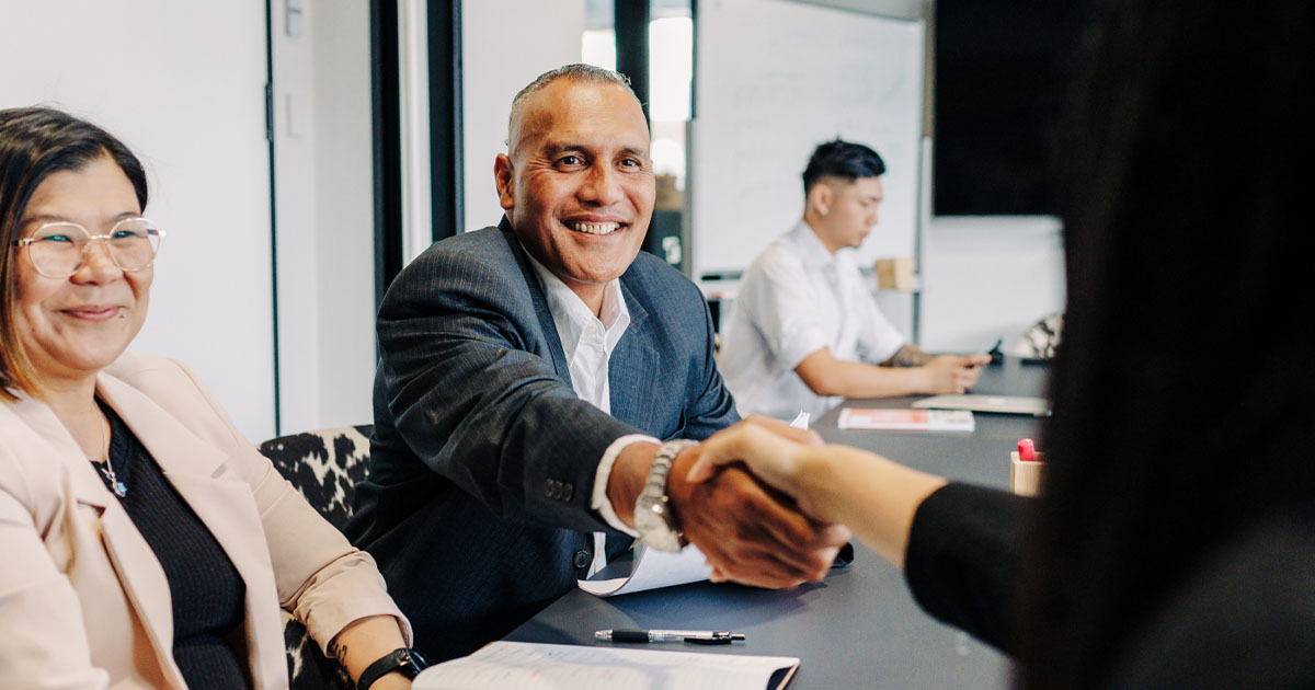 Māori employer reaching out to shake hands with a woman employee sitting next to him