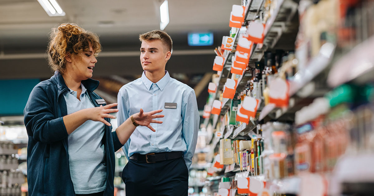 Woman with curly hair who is the store manager giving directions to a young new male employee