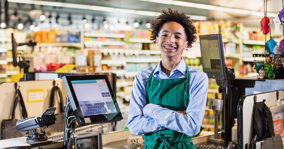 young male teenager with braces wearing an apron is a checkout operator in a supermarket